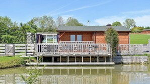 Une cabane en bois dotée d’une terrasse donnant sur un étang.