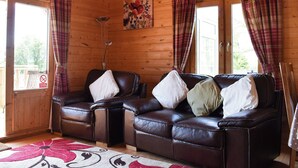 L’intérieur d’un chalet en bois, avec un canapé en cuir, des rideaux à carreaux et un tableau représentant des motifs floraux.