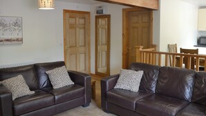 A living room with two dark leather sofas, wooden doors, a wooden ceiling beam, and a dining area with a table and chairs. - 2 bedroom accommodation in Penygroes, near Caernarfon (Penygroes, near Caernarfon)