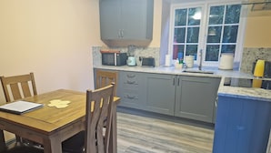 A compact kitchen with grey cabinets, a wooden dining table, and a window with a view of trees. - 2 bedroom accommodation in Penygroes, near Caernarfon (Penygroes, near Caernarfon)
