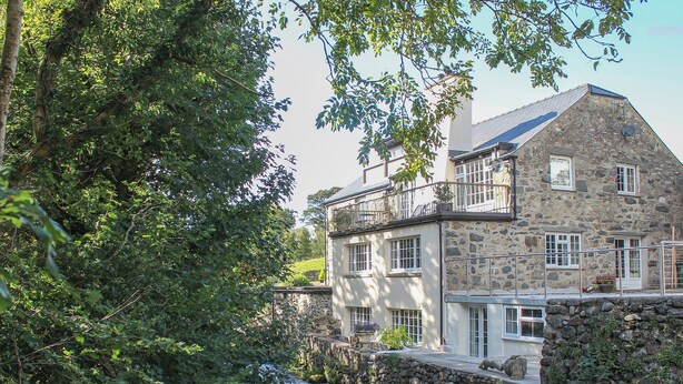 A stone building with a balcony overlooking a river, surrounded by lush greenery. - 2 bedroom accommodation in Penygroes, near Caernarfon (Penygroes, near Caernarfon)
