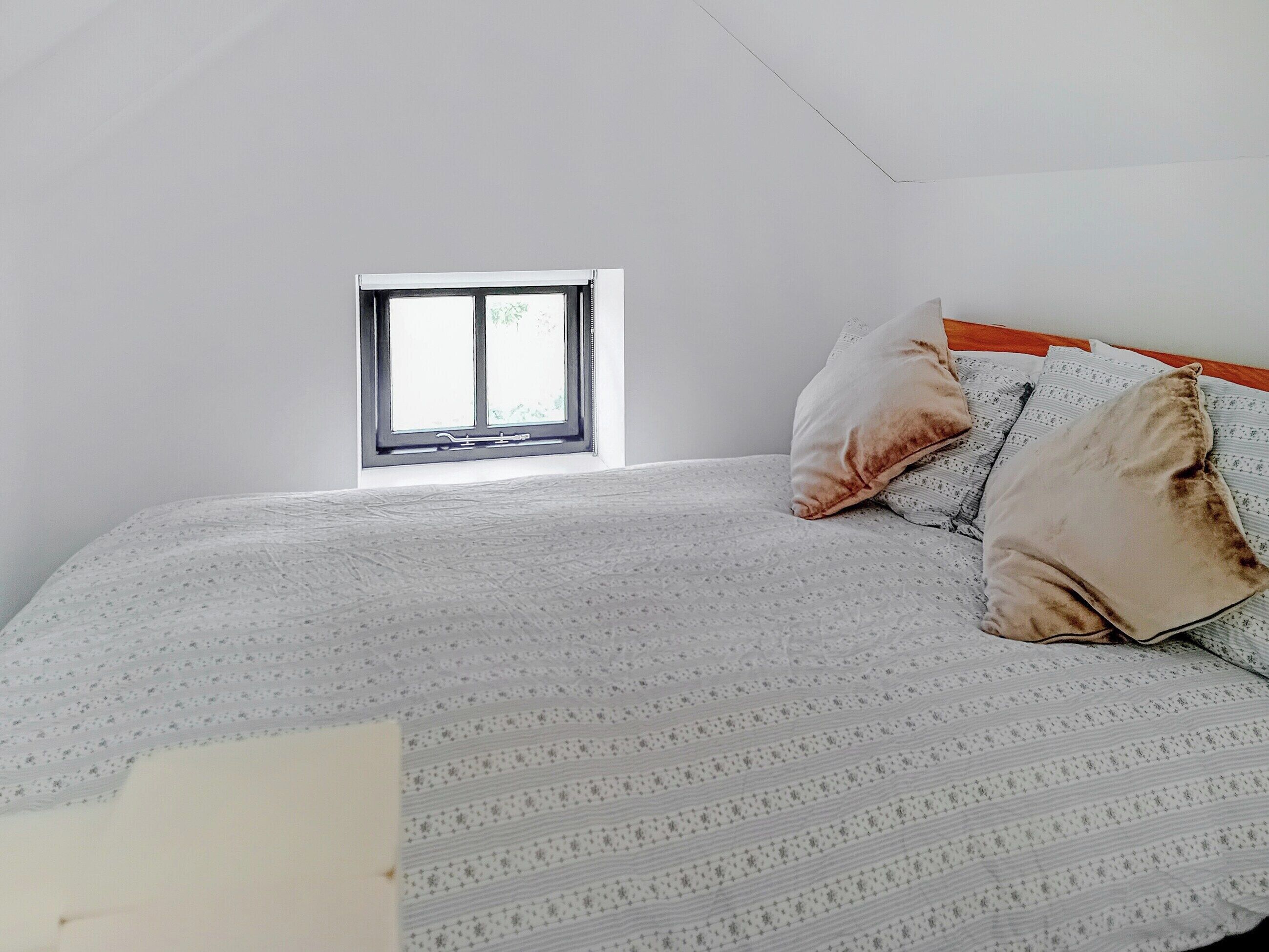 A bedroom with a bed, pillows, a window, and a bedside table.