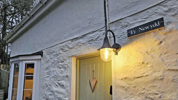 Un edificio con puerta verde, una ventana y una señal de calle que dice 'Ty Newydd'.