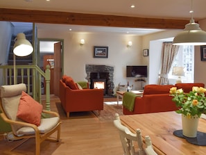 Un salon chaleureux avec une cheminée, des meubles en bois et un escalier menant à l’étage supérieur.