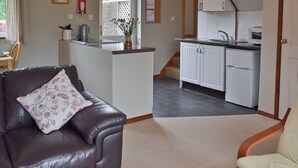 A living room with a brown leather sofa, a beige armchair, and a kitchen area with white cabinets and a refrigerator. - 1 bedroom accommodation in Rye (Rye)