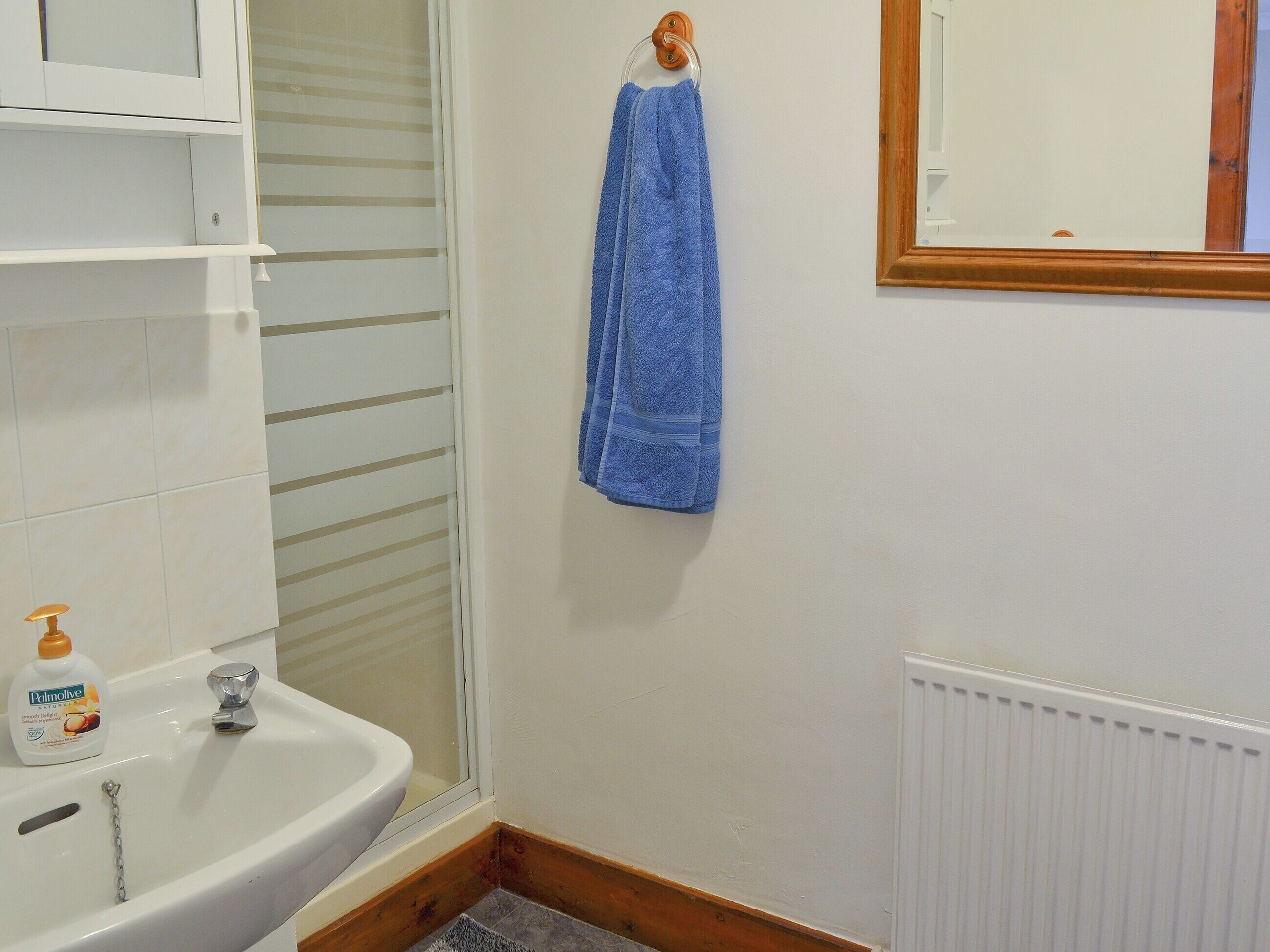 Een badkamer met een witte wastafel, een blauwe handdoek aan de muur en een fles Palmolive zeep.