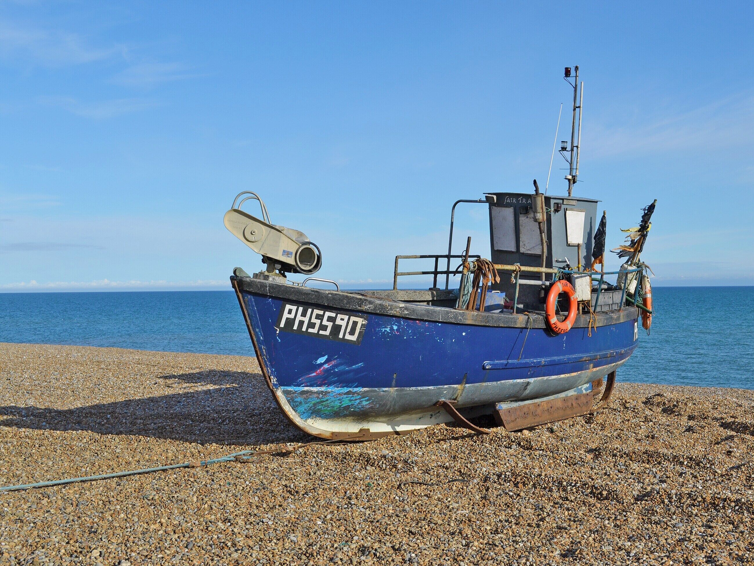 Un bateau de pêche bleu, portant le numéro d’immatriculation PH5590, est amarré sur une plage de galets.