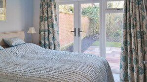 Ein Schlafzimmer mit Bett, Nachttisch, Lampe und Blick durch eine Glastür in einen Garten.