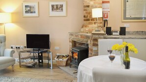 Ein Wohnzimmer mit Kamin, Fernseher und einem Tisch mit Weingläsern und Blumen.