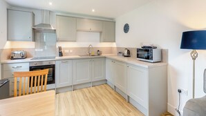 Una cocina moderna con tostadora, microondas, lavaplatos y una silla de madera.