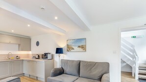 Una cocina moderna con armarios blancos, un área de comedor con sofá gris y una escalera que sube a otro nivel.