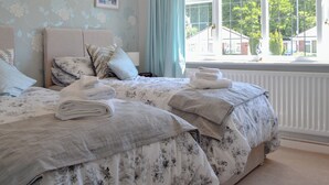 Un dormitorio con dos camas, ropa de cama floral, un cuadro en la pared y vistas al verdor exterior.