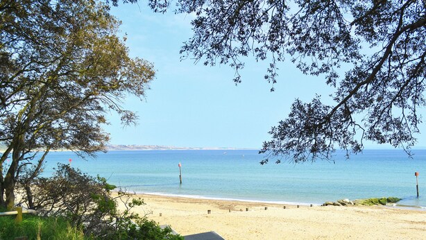 Vista de una playa con cielo despejado, orilla arenosa y una hilera de pequeñas cabañas de playa de color claro.