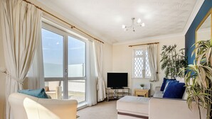 Ein Wohnzimmer mit einer Couch, einem Fernseher, einem Couchtisch und einem großen Fenster mit Vorhängen.