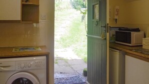 Une cuisine compacte équipée d’un lave-linge, d’un four à micro-ondes et d’une porte verte donnant sur un jardin.