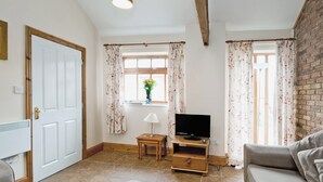 A living room with a sofa, a television on a wooden stand, a small table with a lamp, and a window with curtains. - 2 bedroom accommodation in Filey (Filey)