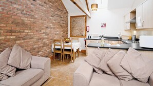 A cozy living room with a brick wall, wooden beams, and a dining area with a table and chairs. - 2 bedroom accommodation in Filey (Filey)