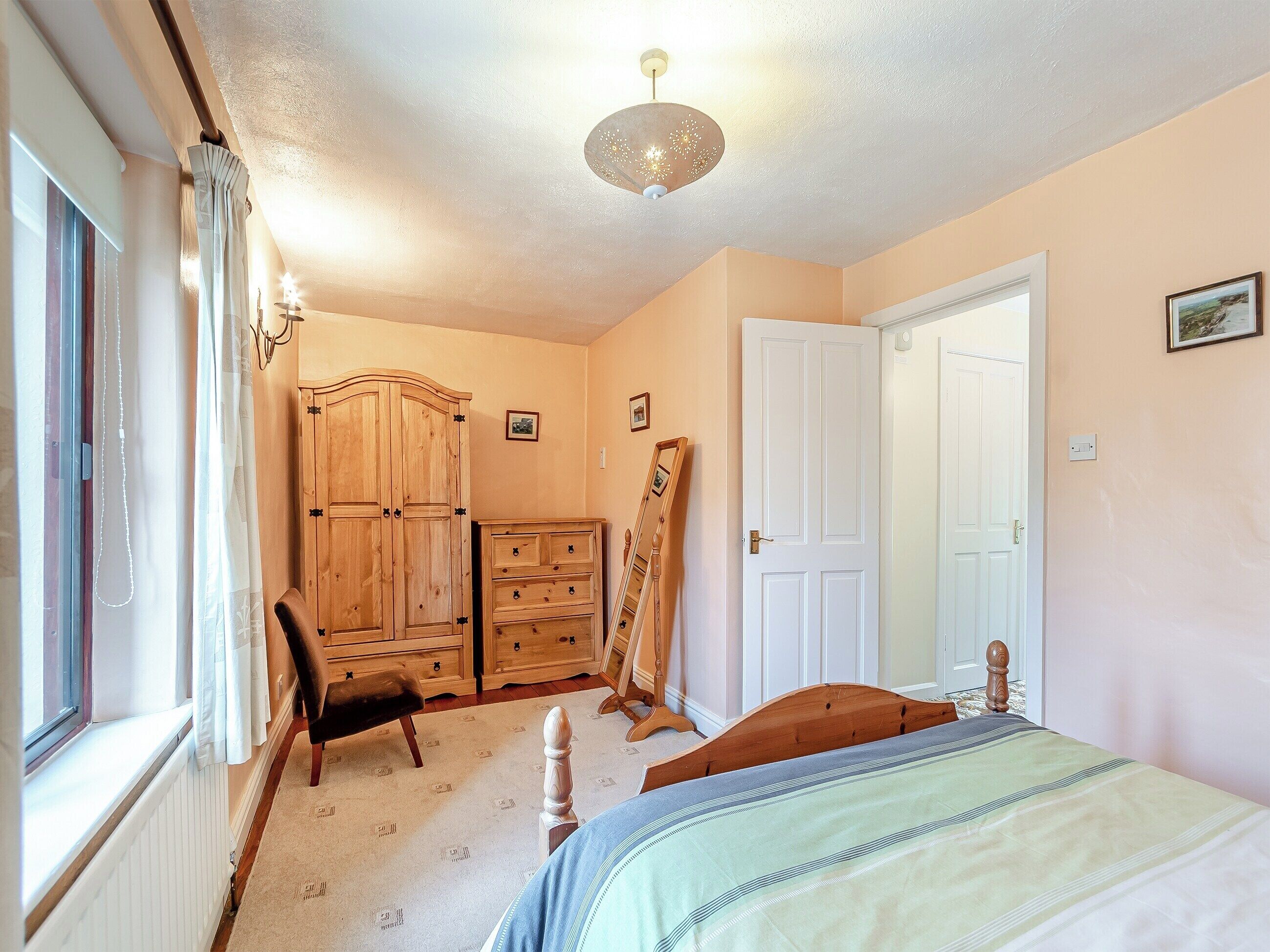 Een slaapkamer met een bed, een houten garderobe, een dressoir, een stoel en een deur.