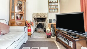 A living room with a white sofa, a wooden cabinet, a fireplace, a bookshelf, and a flat-screen TV. - 2 bedroom accommodation in Darley Bridge, near Matlock (Darley Bridge, near Matlock)