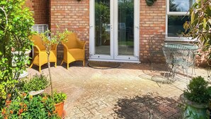 Ein Ziegelhaus mit Terrasse, gelben Stühlen und Blumentöpfen.