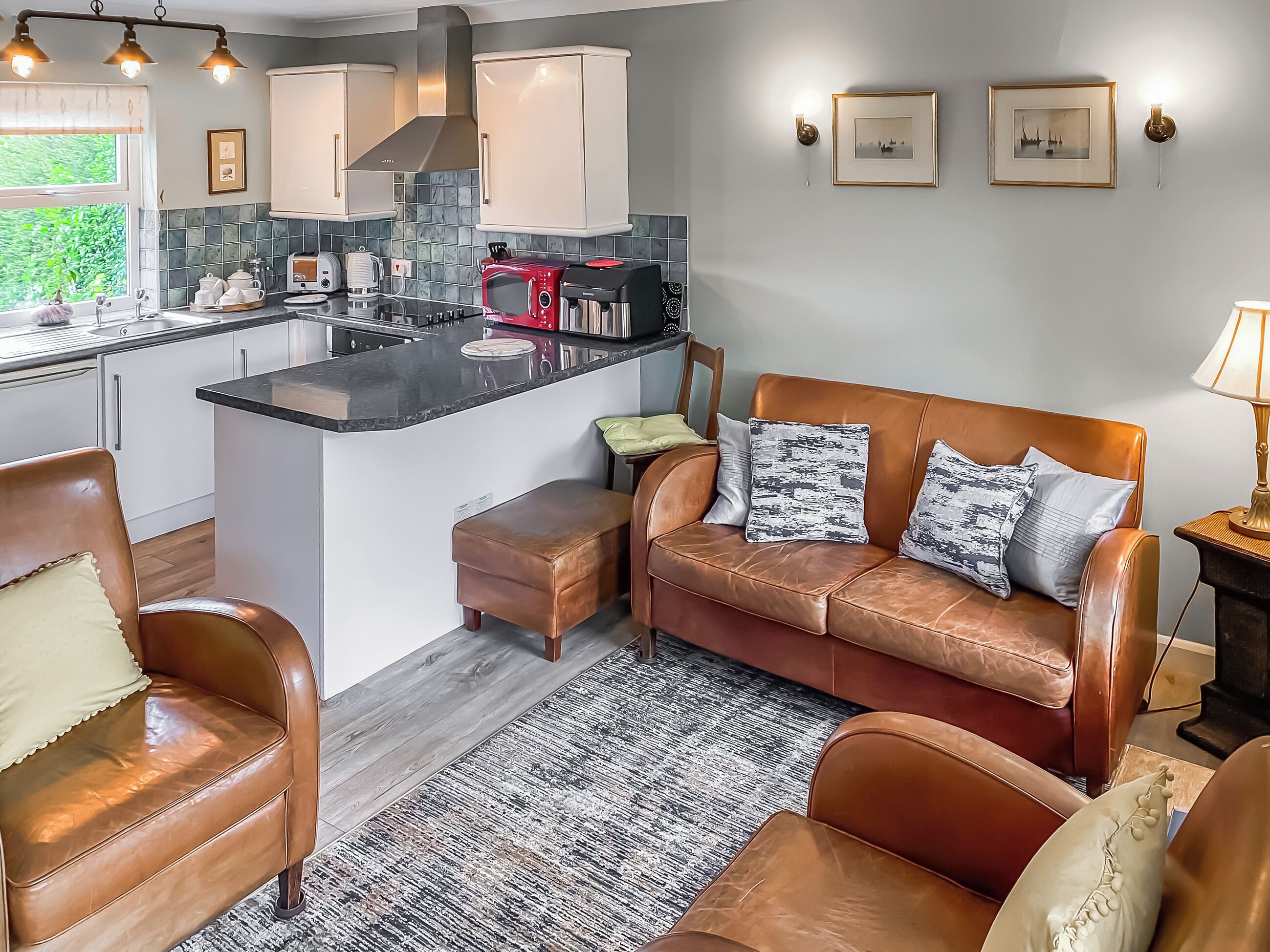 A modern kitchen with a central island, a brown leather sofa with patterned cushions, and a wooden floor.