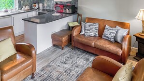 Eine moderne Küche mit einer zentralen Kochinsel, ein braunes Ledersofa mit gemusterten Kissen und ein Holzboden.