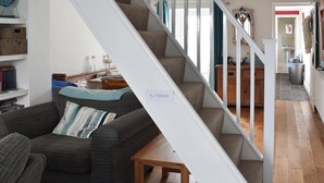 A staircase leading to a second floor, a living room with a sofa and a table, and a kitchen area with cabinets and a sink.