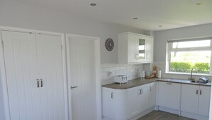 Une cuisine avec des meubles blancs, une chaise en bois et une fenêtre donnant sur un paysage verdoyant.