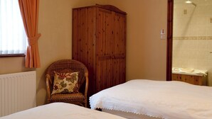 A bedroom with two beds, a wooden wardrobe, a wicker chair, and a window with curtains.