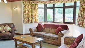 A living room with a brown leather sofa, patterned armchairs, a wooden coffee table, and floral curtains.