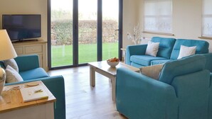 Ein Wohnzimmer mit blauem Sofagarnitur, einem Fernseher und einer großen Schiebeglastür, die in einen Garten führt.