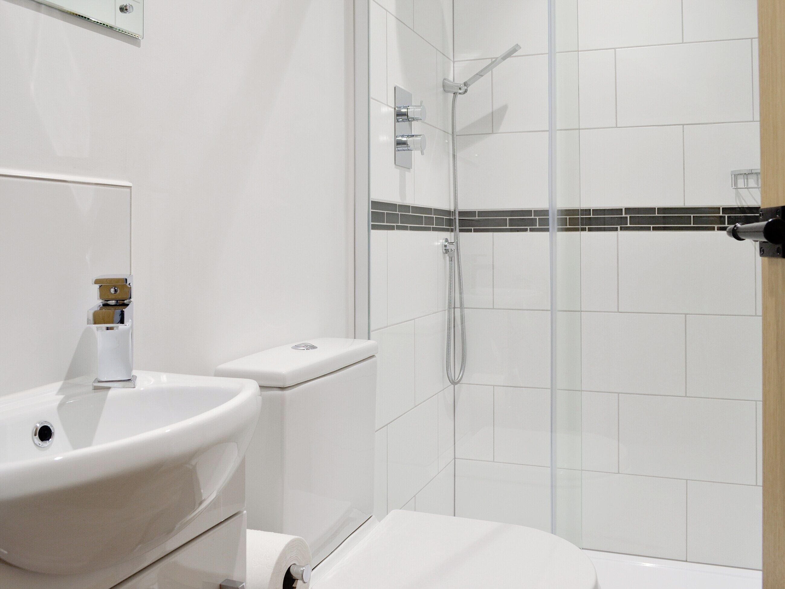 Un baño moderno con lavamanos, inodoro y zona de ducha blancos.