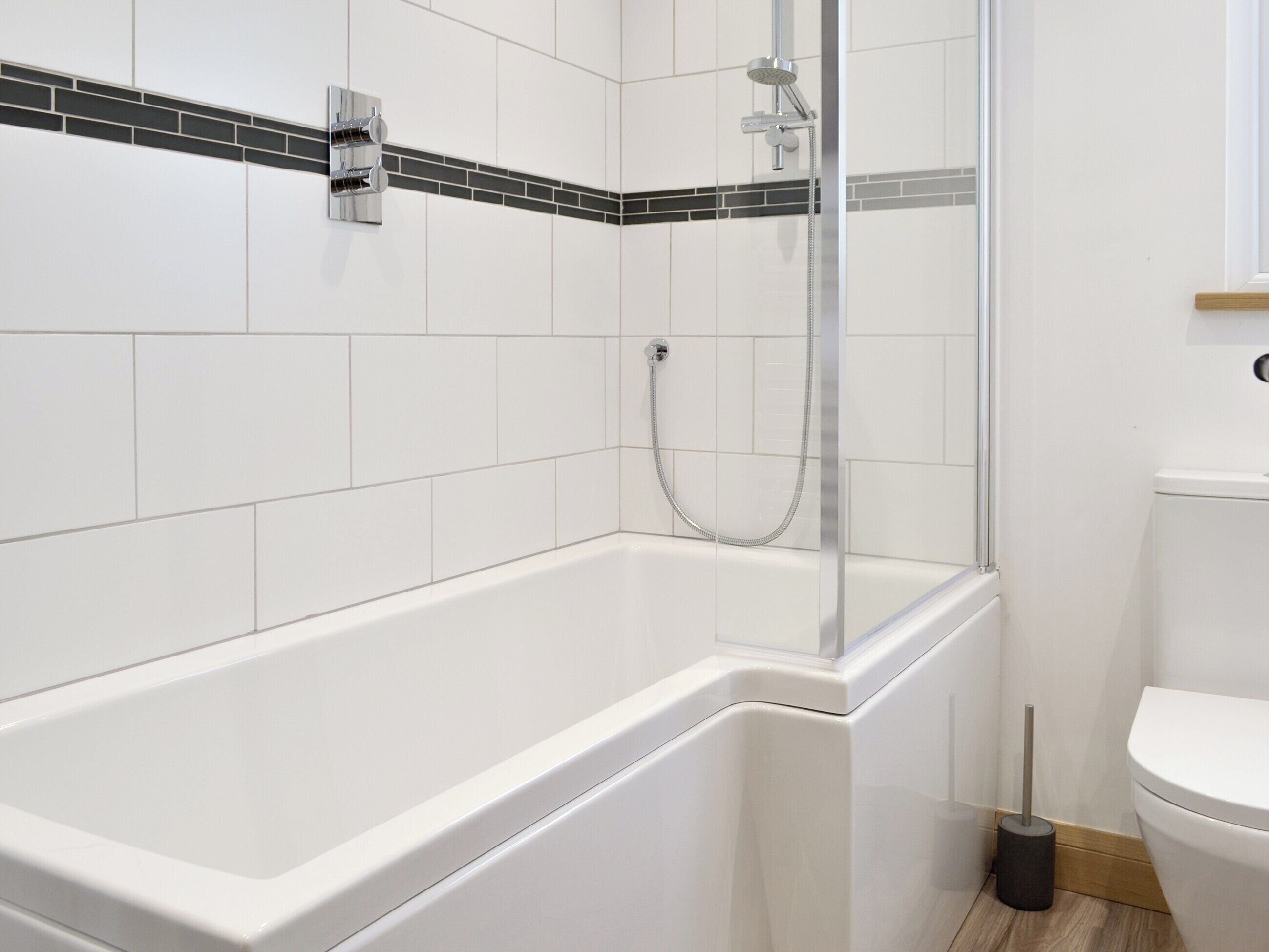 Ein modernes Badezimmer mit einer weißen Badewanne, einer Glaskabinentasse und einer Toilette.
