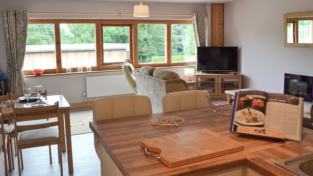 A modern kitchen with a wooden island, dining area, and large windows offering a view of the outdoors. - 2 bedroom accommodation in Cutthorpe, near Chesterfield (Cutthorpe, near Chesterfield)