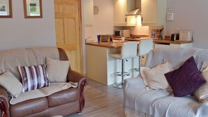 A living room with a brown leather sofa, a white armchair, and a wooden door. - 2 bedroom accommodation in Cutthorpe, near Chesterfield (Cutthorpe, near Chesterfield)