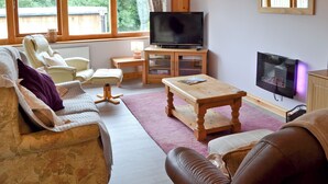 A living room with a sofa, armchair, wooden coffee table, and a television on a stand. - 2 bedroom accommodation in Cutthorpe, near Chesterfield (Cutthorpe, near Chesterfield)