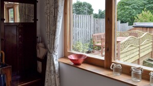A room with a window overlooking a garden, a wooden bench, and a red bowl on the windowsill. - 2 bedroom accommodation in Cutthorpe, near Chesterfield (Cutthorpe, near Chesterfield)
