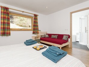 A bedroom with a bed, a bedside table, a red sofa, a window with curtains, and a shower area.