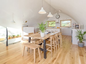 Een moderne keuken met houten vloeren, een eettafel met stoelen, hanglampen en uitzicht op het buitengebied.