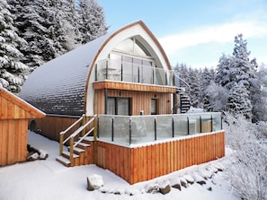 A wooden cabin with a glass balcony, a staircase, and a snow-covered landscape.