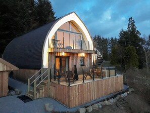 A wooden cabin with a curved roof, a balcony with seating, and a staircase leading to an upper level.