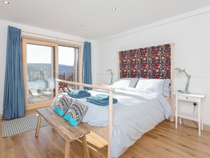 A bedroom with a bed, a bench, a desk, and a large window.