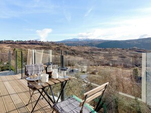 A wooden deck with a table set for dining, overlooking a mountainous landscape. - Jill Strawbale House- UKC2935 (Strontian, near Fort William)