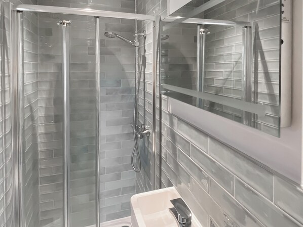 Una ducha con paredes de cristal, con grifo y ducha de cromo, junto a un lavabo blanco con grifo de cromo.