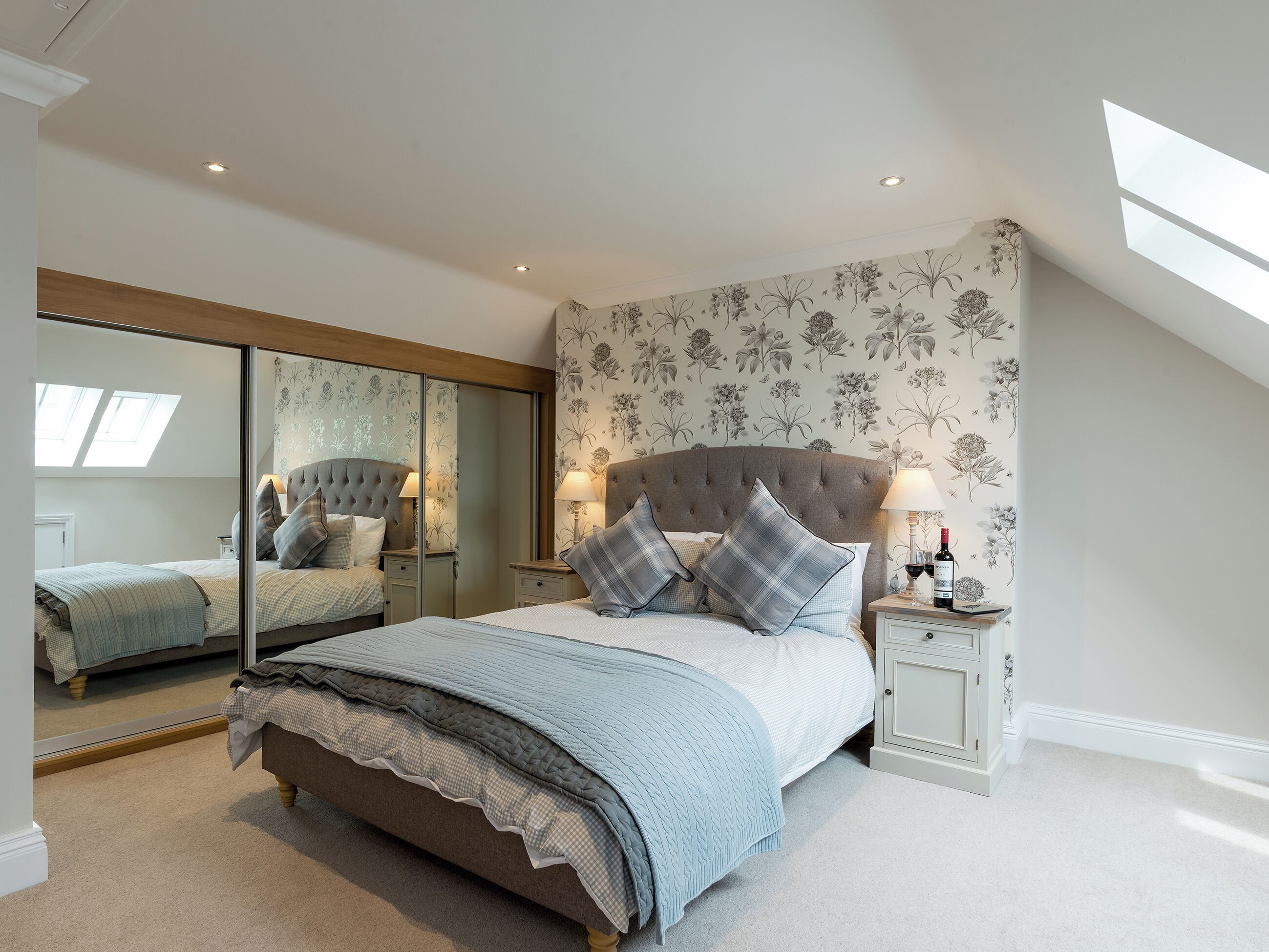 A bedroom with a large bed, two bedside tables, a mirror, and a skylight.