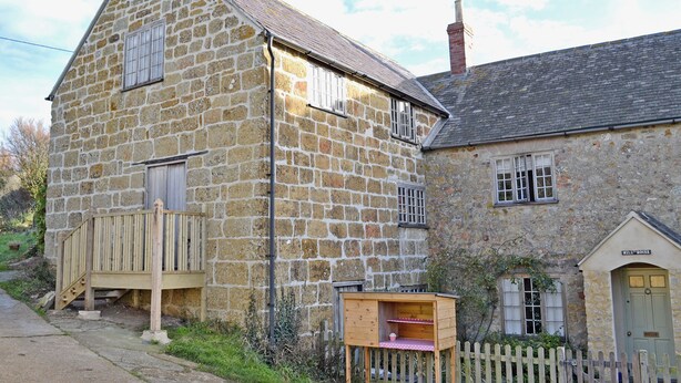 A stone building with a wooden deck and a small wooden structure with a pink roof. - Millstones is a lovely property for two. (Seatown, Chideock)