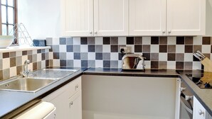 A kitchen with white cabinets, a black and white tiled backsplash, a toaster, and a sink. - Millstones is a lovely property for two. (Seatown, Chideock)