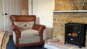 A leather armchair with a cushion labeled "Charleston Polo" and a black wood-burning stove with a stone shelf above it. - Millstones is a lovely property for two. (Seatown, Chideock)