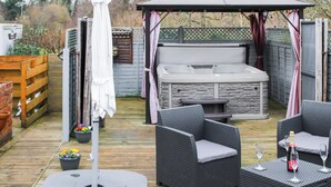 En terrasse med udendørs møbler, jacuzzi og plantekasser.