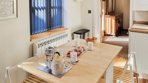 Et spiseområde med et træbord, hvide stole, en kaffekande og en skål med frugt.